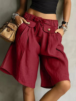 A lady wearing burgundy High-Waisted Drawstring Shorts  posing on a white wall