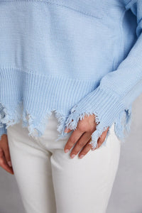 Light blue knitted sweater with distressed edges worn by a person on a neutral background