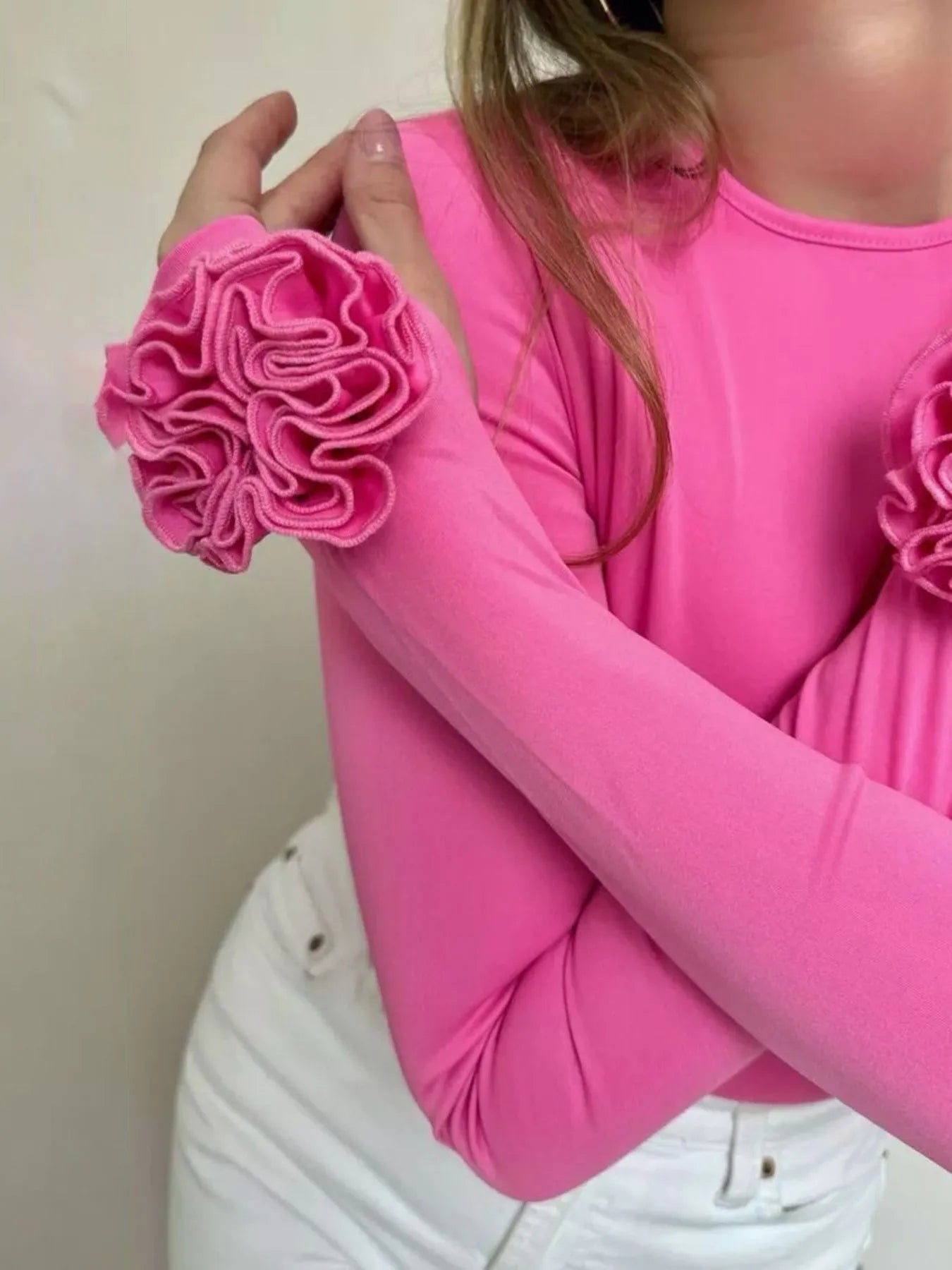 Person wearing a pink long-sleeve top with floral designs on a plain background