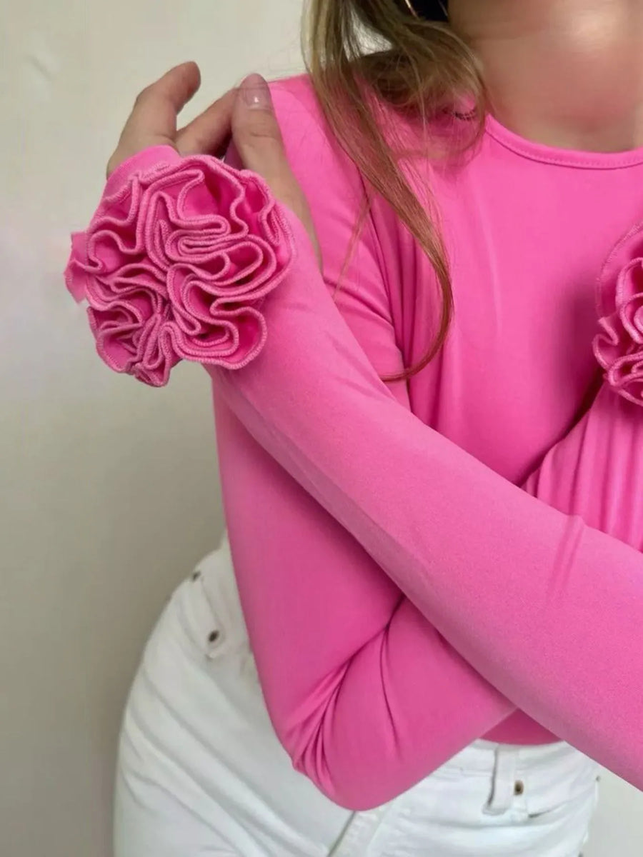 Person wearing a pink long-sleeve top with floral designs on a plain background