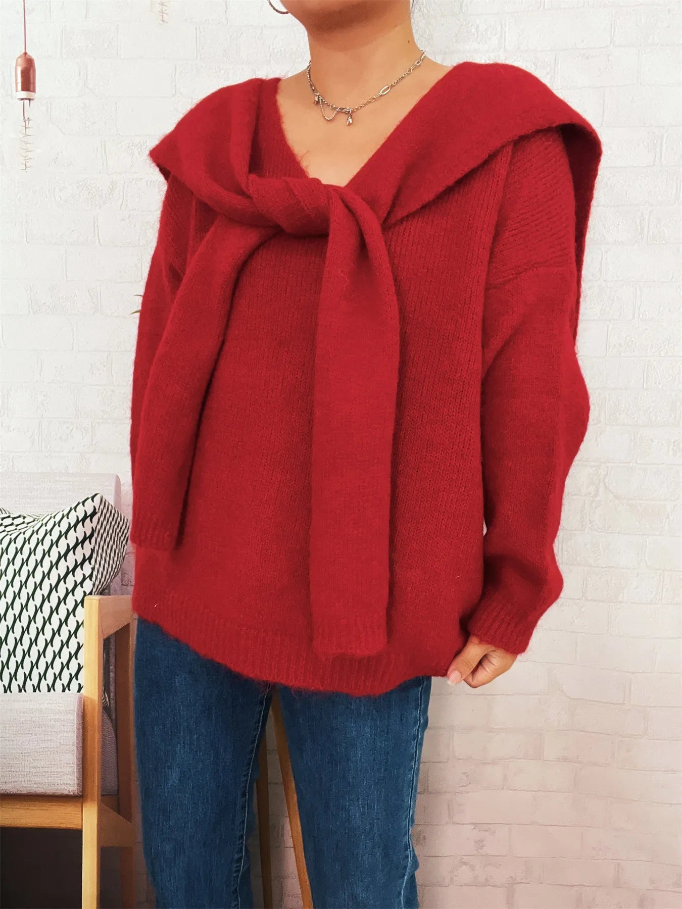 Person wearing a red sweater with a large bow in front of a white brick wall.