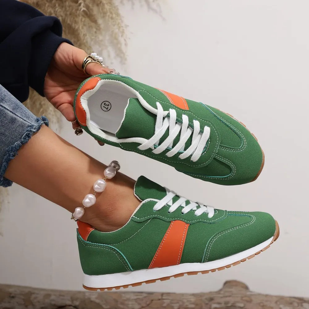 Green sneakers with orange accents held by a person wearing a pearl bracelet.