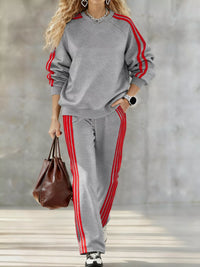 Person wearing a gray tracksuit with red stripes holding a brown bag against a neutral background