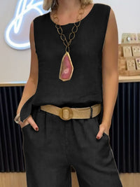 Person wearing a black sleeveless top with a large pendant necklace and high-waisted black pants.