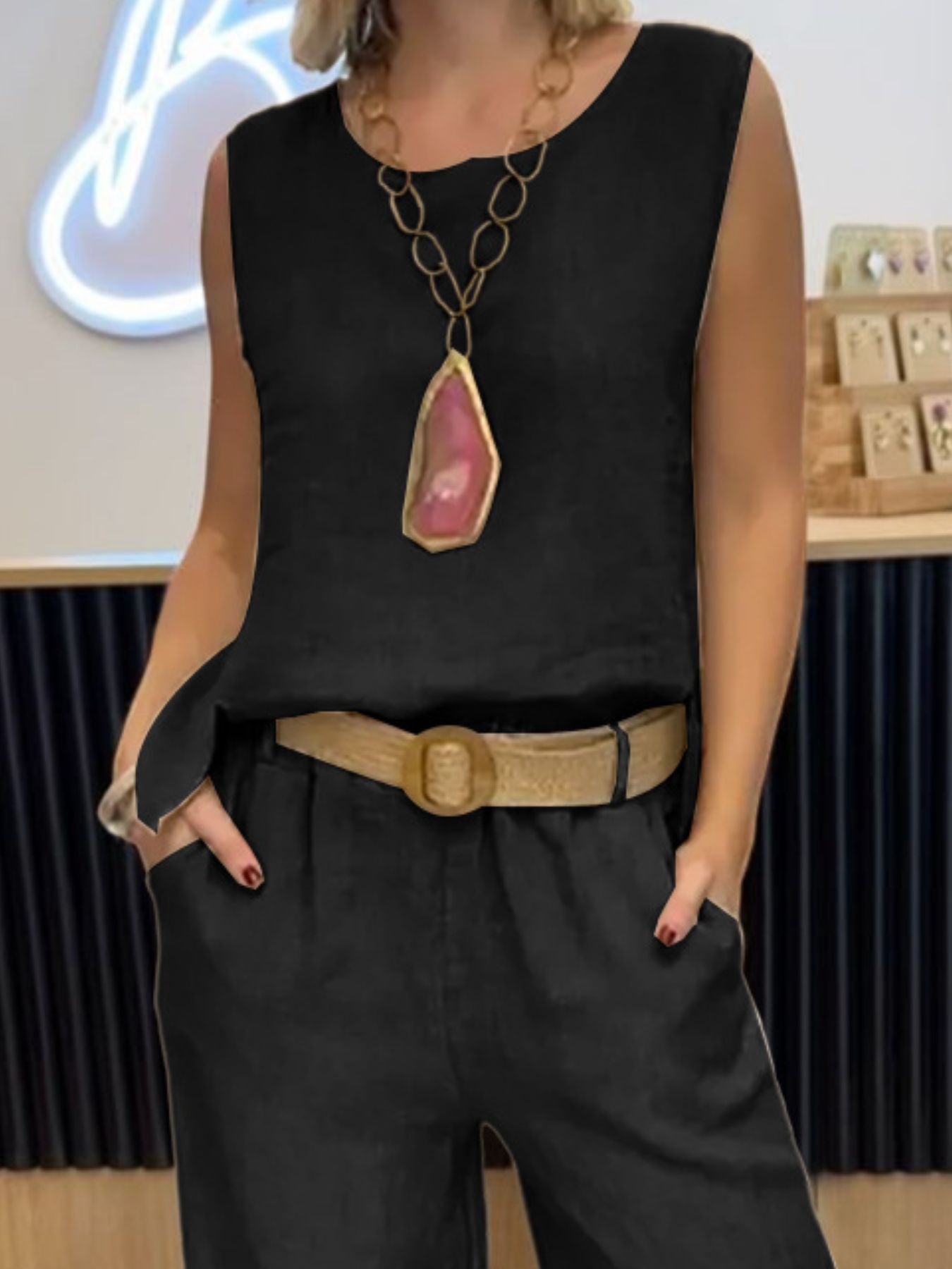 Person wearing a black sleeveless top with a large pendant necklace and high-waisted black pants.