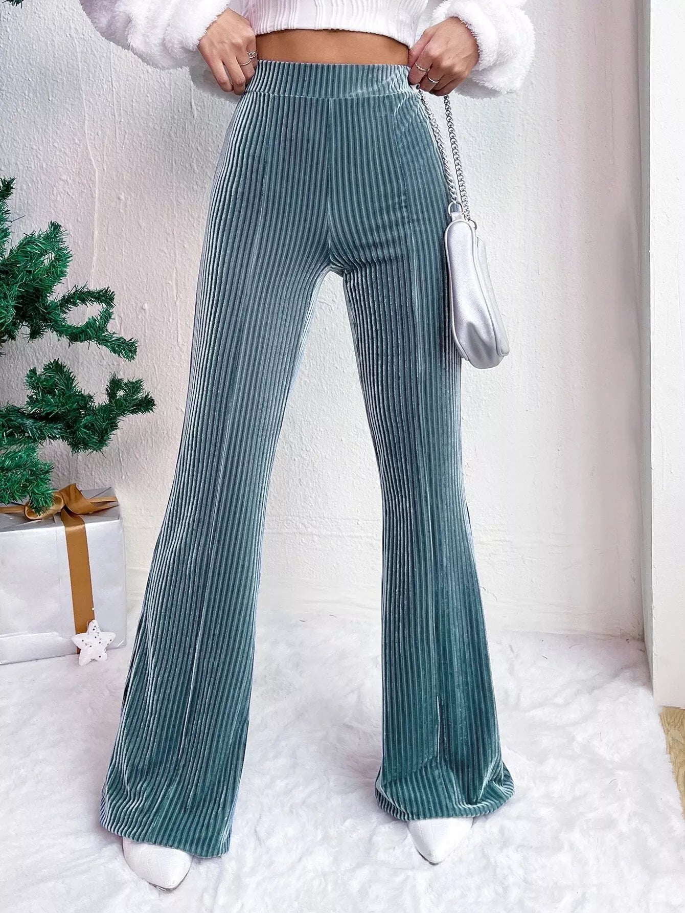 Person wearing teal velvet flared pants with a white background