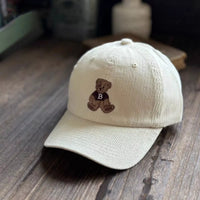 Beige cap with teddy bear emblem on a wooden surface