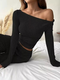 Person wearing a black off-shoulder ribbed top sitting on a bed.