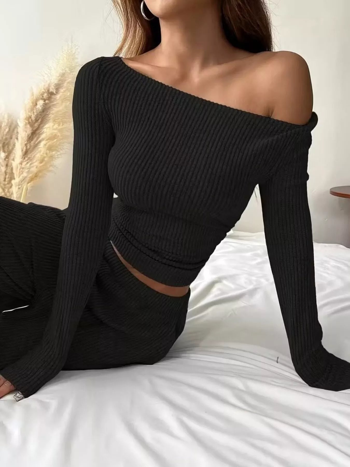 Person wearing a black off-shoulder ribbed top sitting on a bed.
