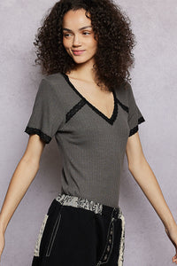 Woman wearing a gray top with black lace trim against a plain background
