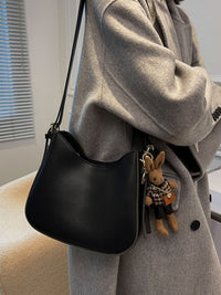 Person wearing a gray coat with a black handbag featuring a plush toy keychain.