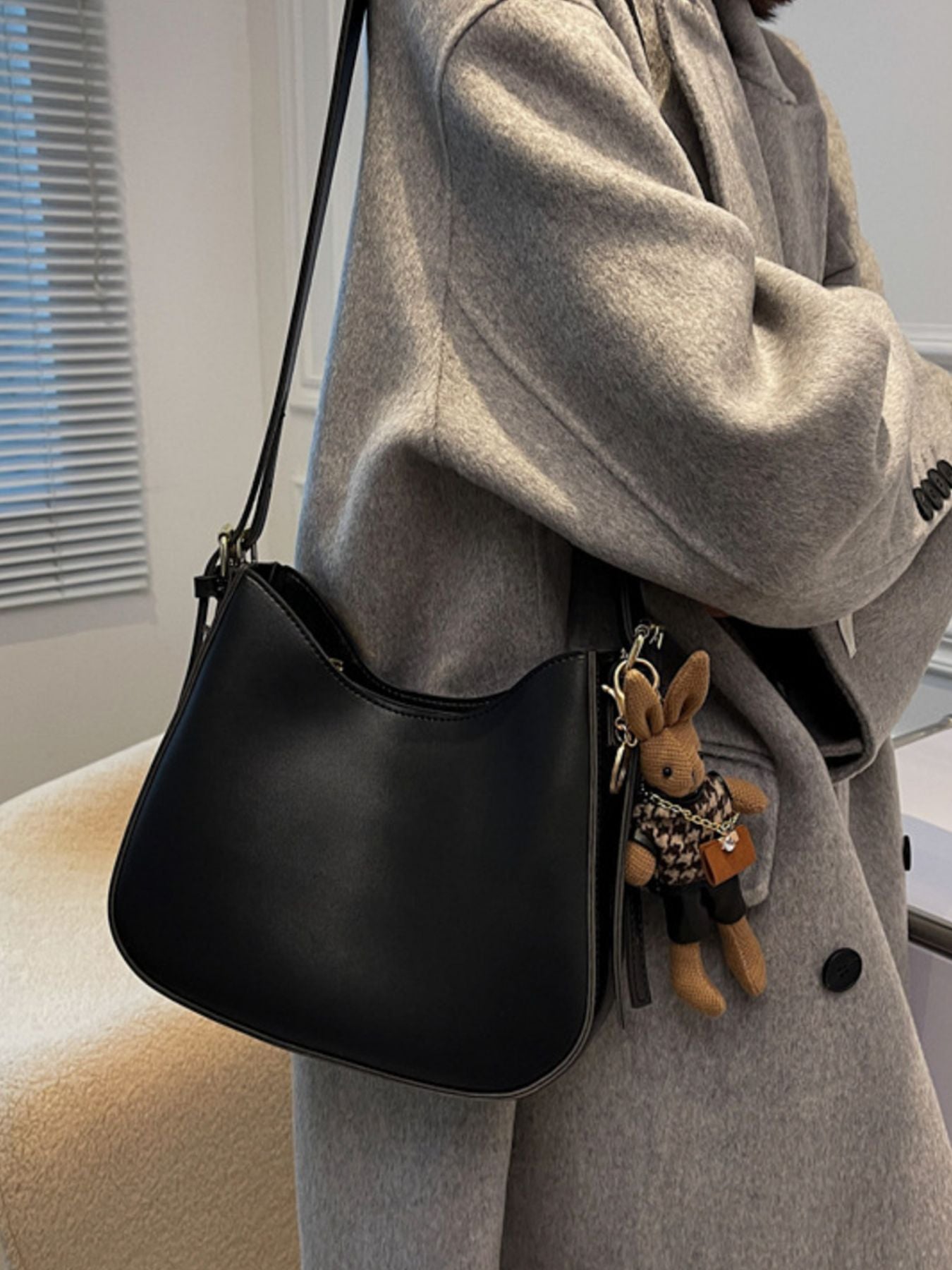 Person wearing a gray coat with a black handbag featuring a plush toy keychain.