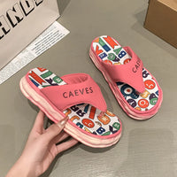 Pink slippers with colorful letter pattern held by a hand on a gray surface.