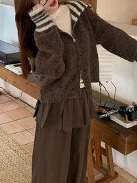 Person wearing a brown cardigan and pants in an indoor setting.