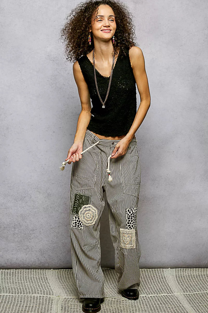 Woman wearing a black sleeveless top and patterned pants against a gray background