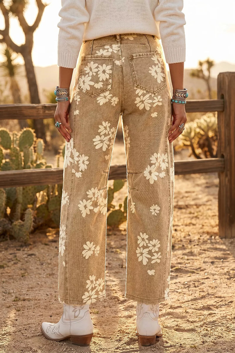 A person standing outdoors in a desert setting wearing tan wide-leg jeans with a white floral print, a cream sweater, and white cowboy boots.