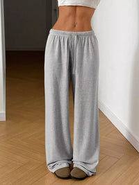 Person wearing gray sweatpants in a room with wooden flooring and white walls.