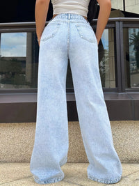 Person wearing light blue jeans standing in front of a building with reflective glass windows.
