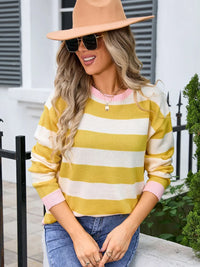 Woman wearing a yellow and white striped sweater with pink accents, blue jeans, and a beige hat outdoors.