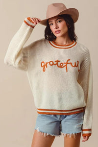 Woman wearing a sweater with 'grateful' text and a hat against a beige background