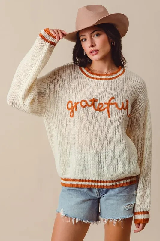 Woman wearing a sweater with 'grateful' text and a hat against a beige background
