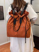 Person wearing an orange drawstring bag over a white shirt in a room.