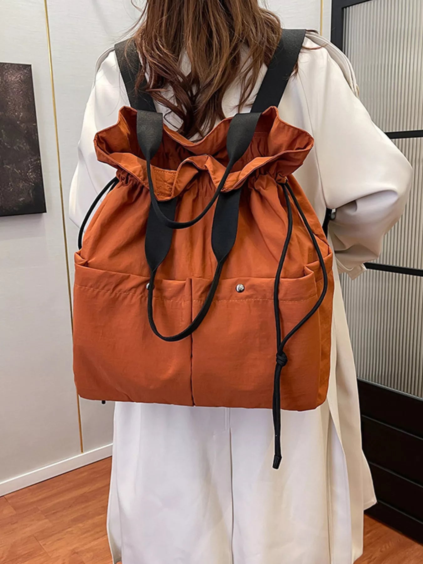Person wearing an orange drawstring bag over a white shirt in a room.