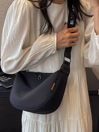 Person holding a black shoulder bag with a visible brand logo.