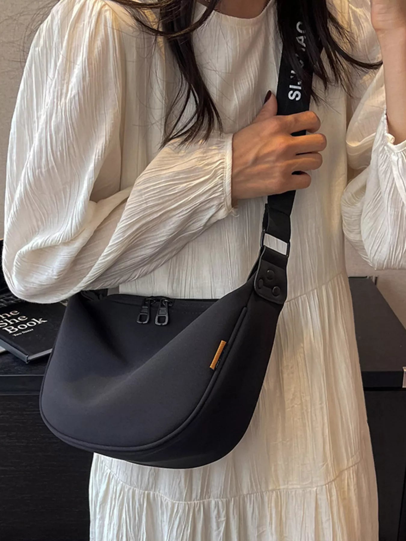 Person holding a black shoulder bag with a visible brand logo.