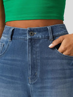 Close-up of blue jeans with a green top worn by a person.