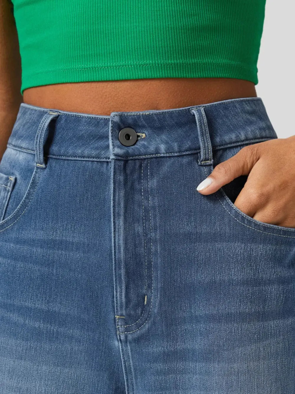 Close-up of blue jeans with a green top worn by a person.