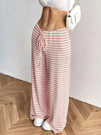 Person wearing pink and white checkered pants on a wooden floor.