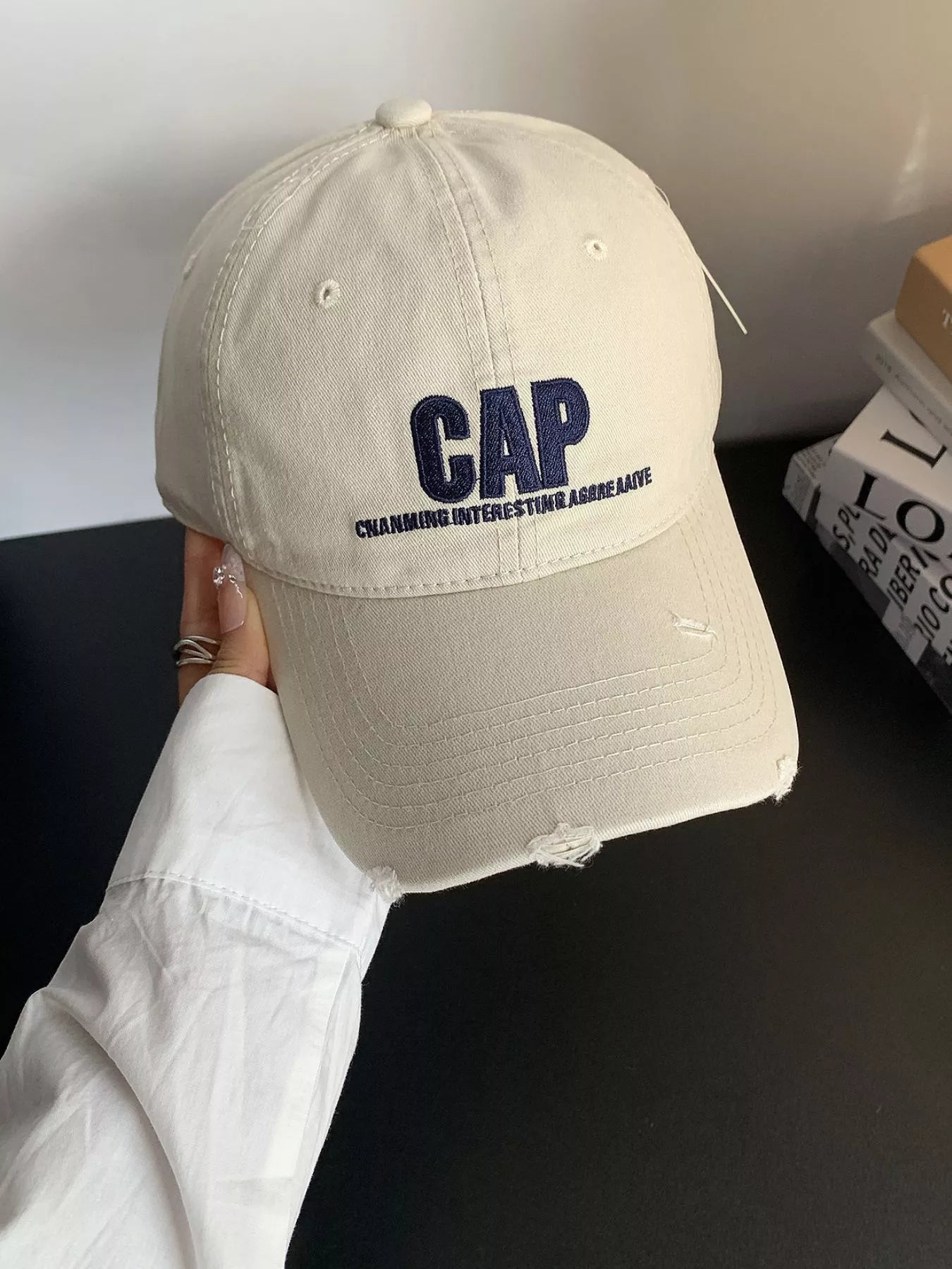 Beige cap with 'CAP' text held by a person against a dark background