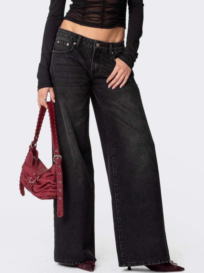 Person wearing black wide-leg jeans and a black top, holding a red handbag on a white background