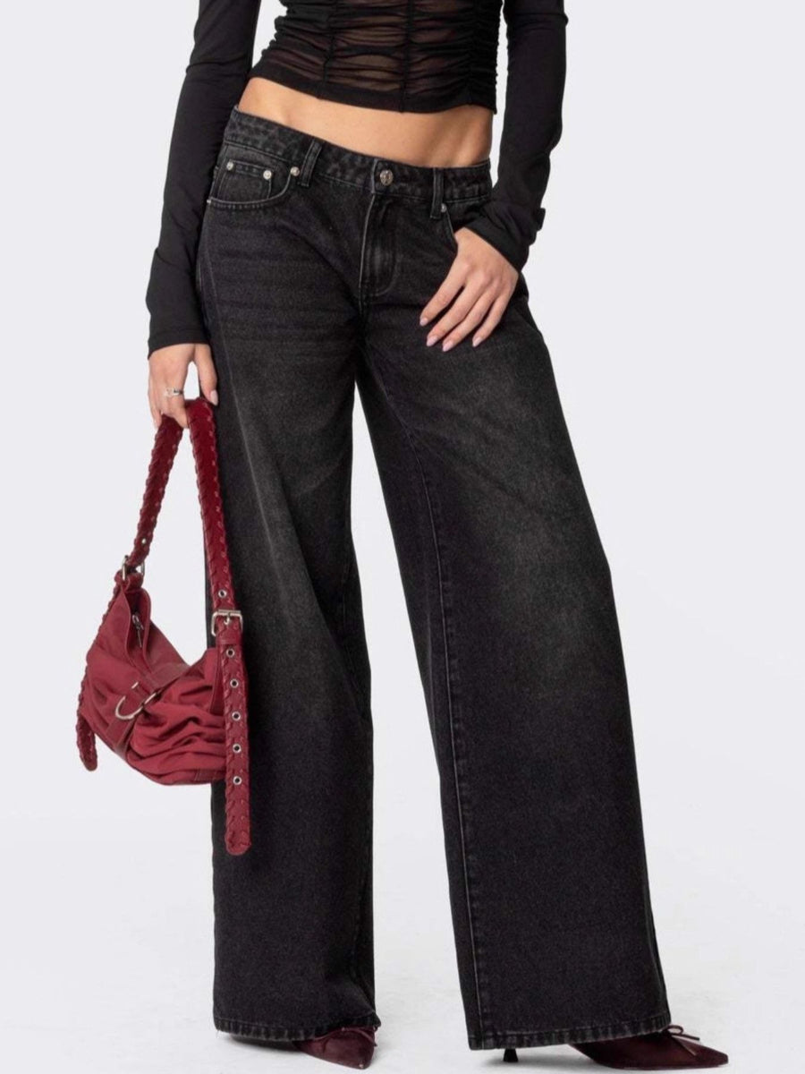 Person wearing black wide-leg jeans and a black top, holding a red handbag on a white background
