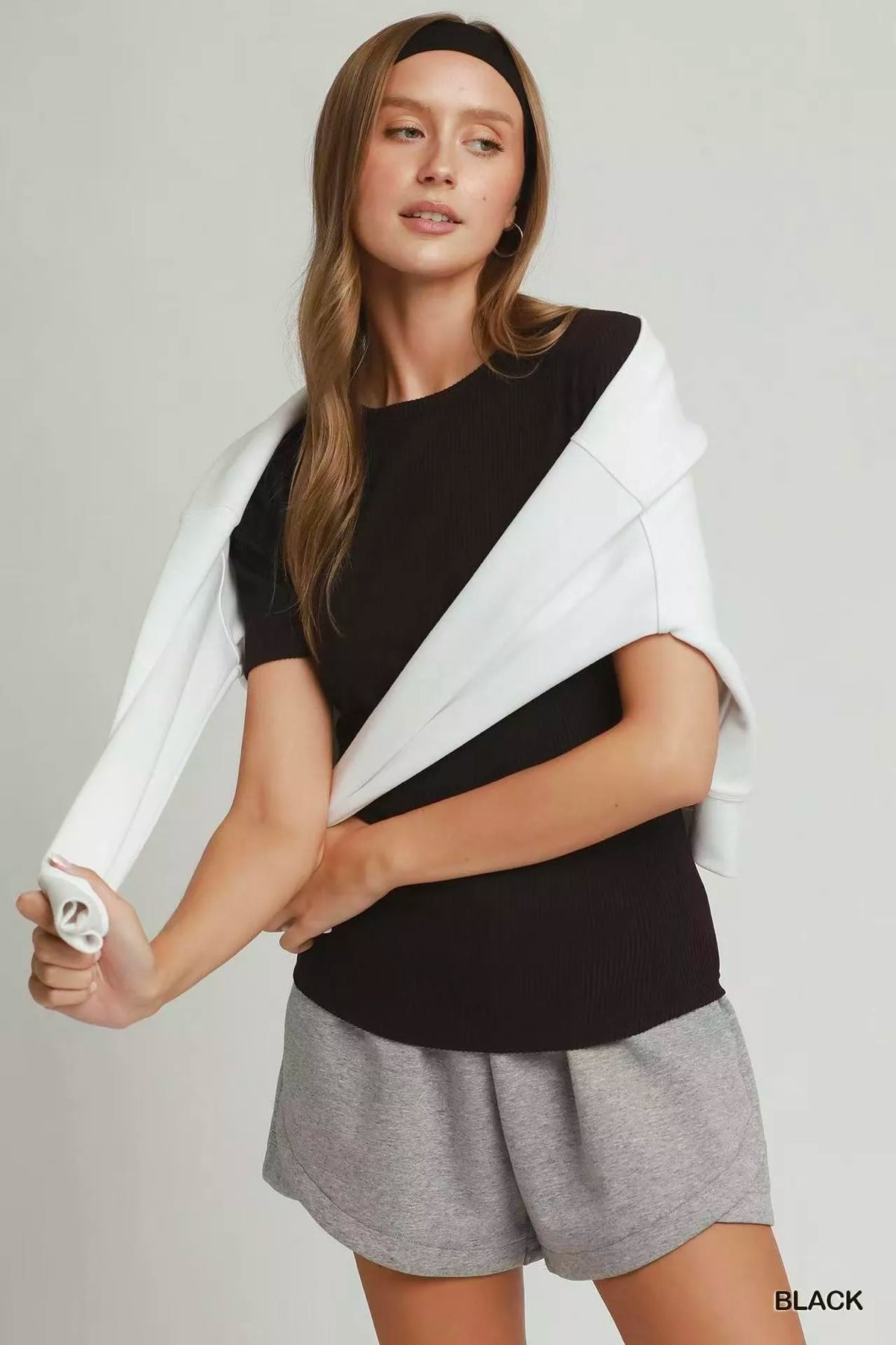 Woman wearing a black and white top with gray shorts on a plain background