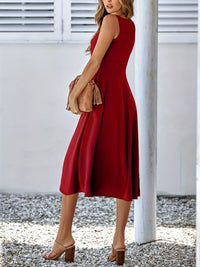 Woman wearing a red dress holding a beige handbag against a white background