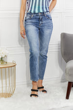 Person wearing blue jeans and a striped top in a room with a white wall and gray chair.