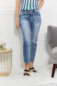 Person wearing blue jeans and a striped top in a room with a white wall and gray chair.