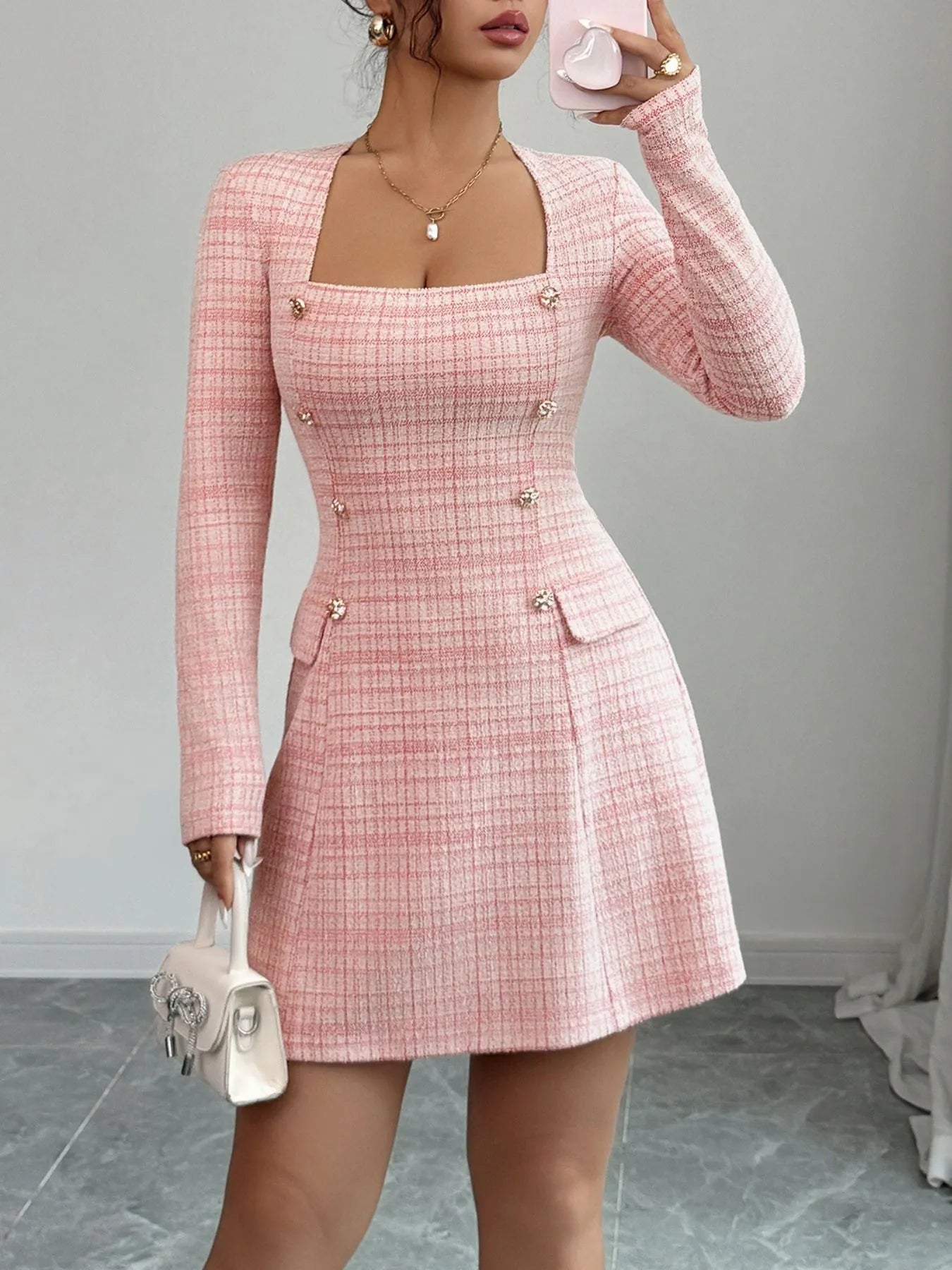 Person wearing a pink checkered dress with long sleeves against a gray background