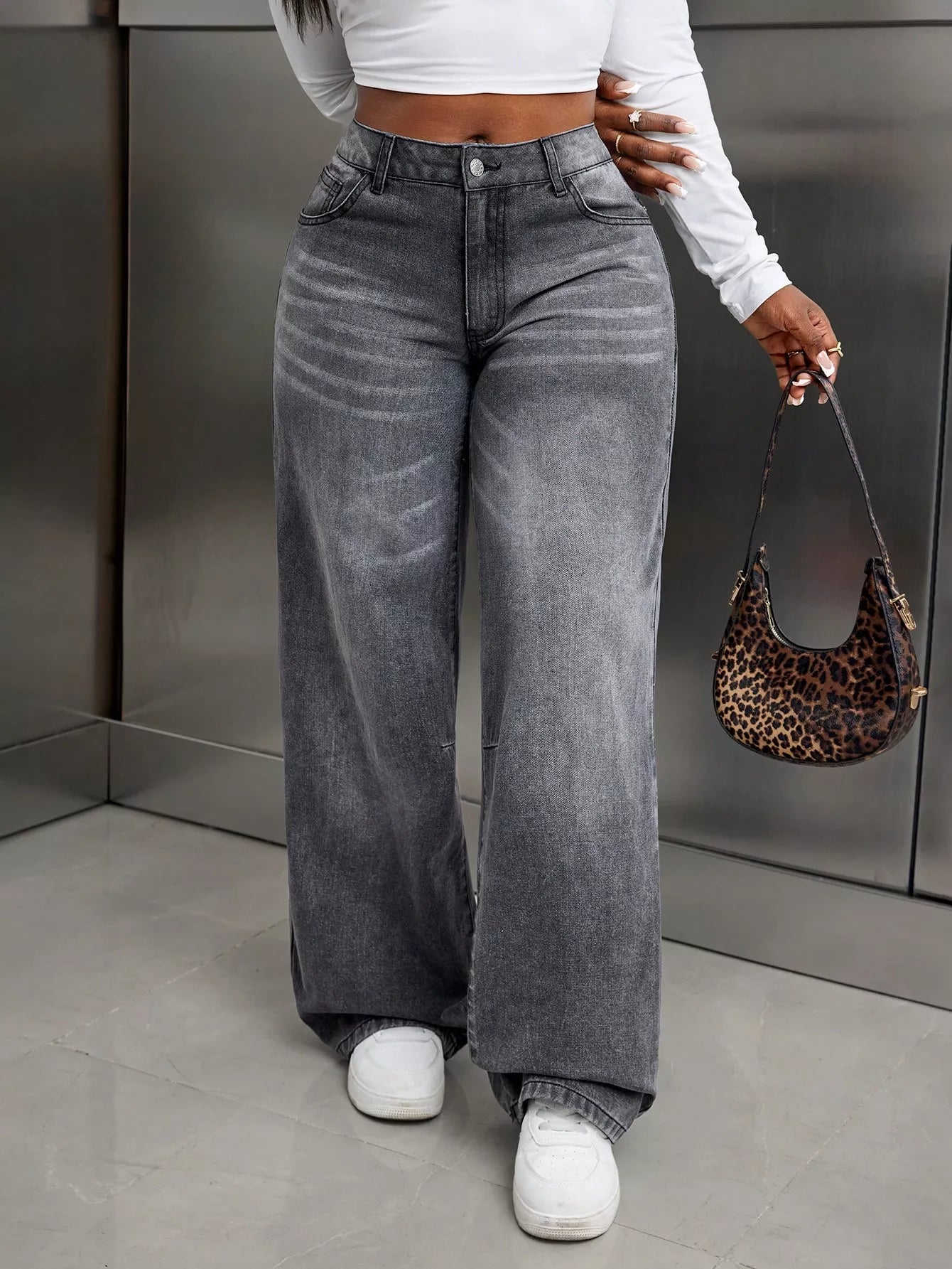 Person wearing gray wide-leg jeans and white sneakers, holding a leopard print handbag.