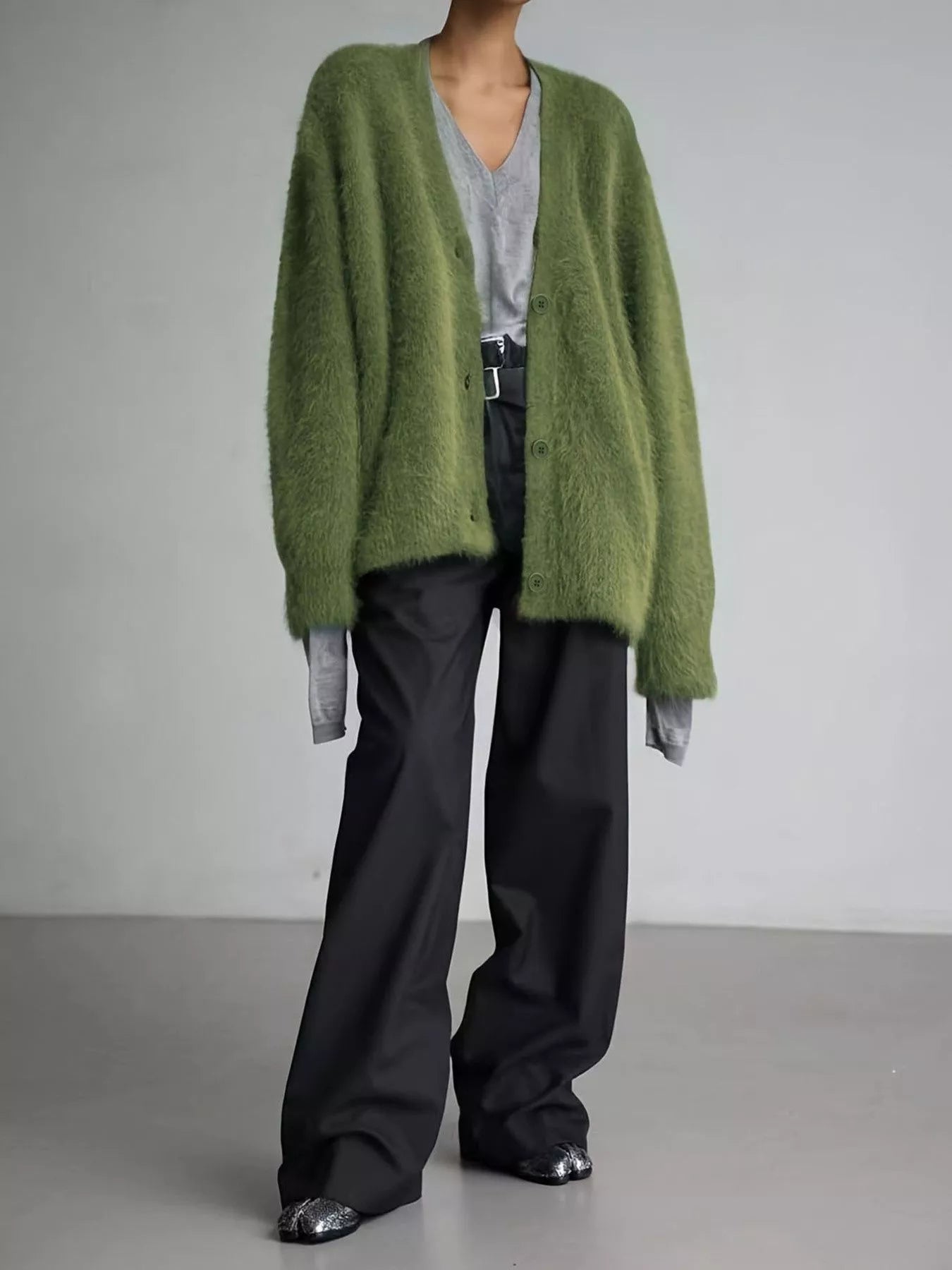 Person wearing a green cardigan, gray shirt, black pants, and black shoes on a plain background