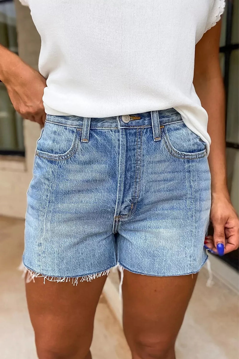 Person wearing light blue denim shorts and a white top indoors.