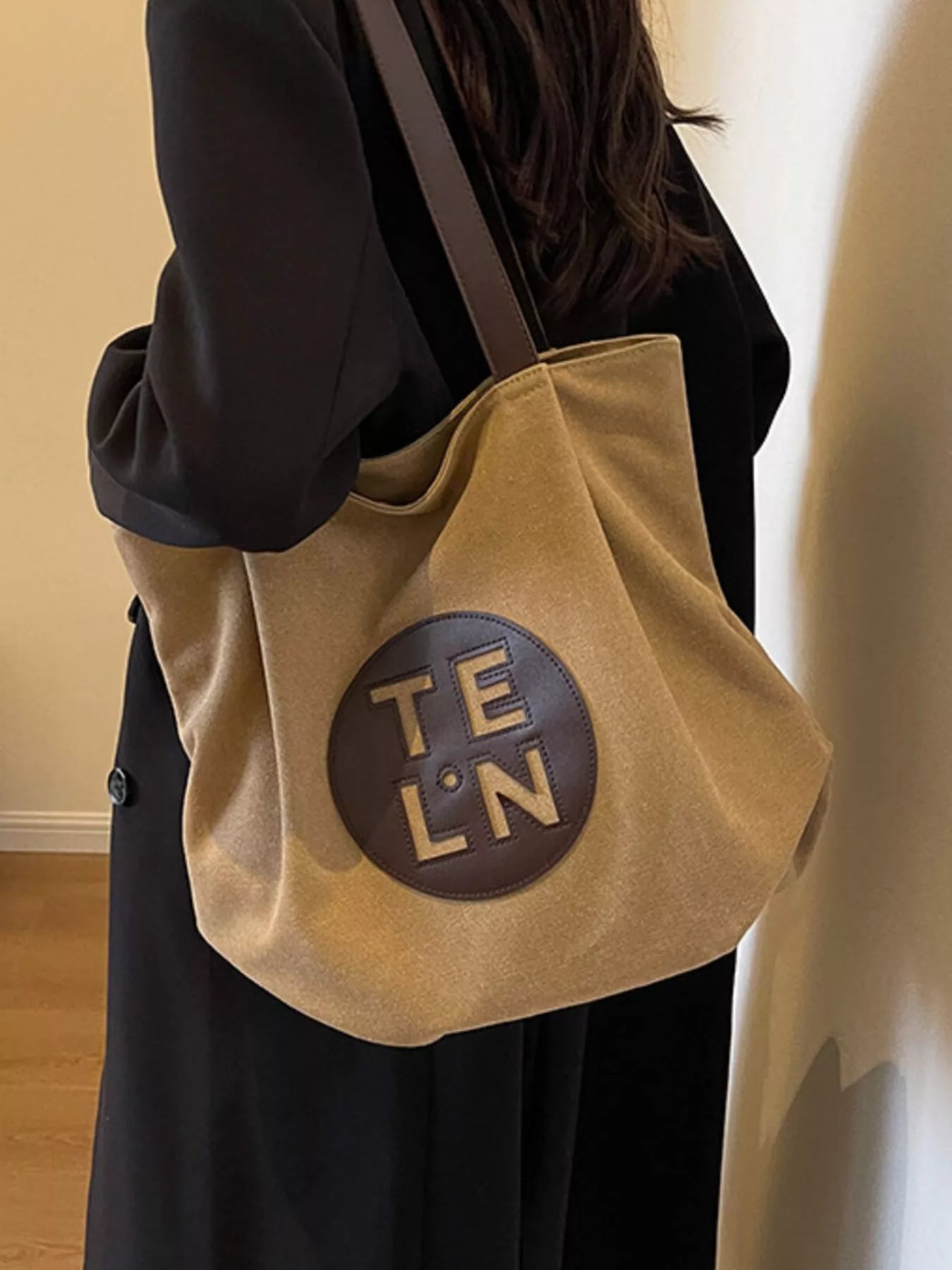 Beige tote bag with 'TE LN' logo worn by a person against a neutral background