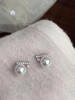 Pearl earrings with silver accents on a textured fabric surface