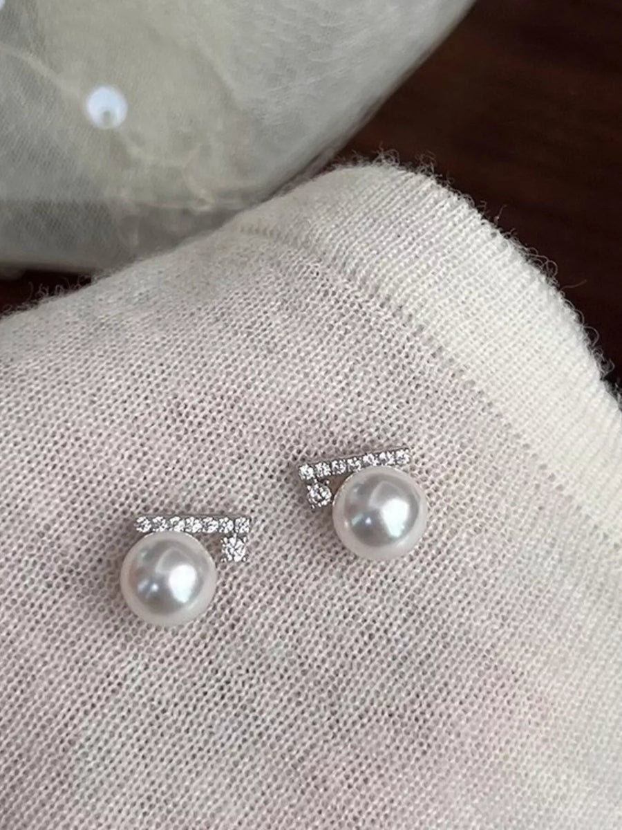 Pearl earrings with silver accents on a textured fabric surface