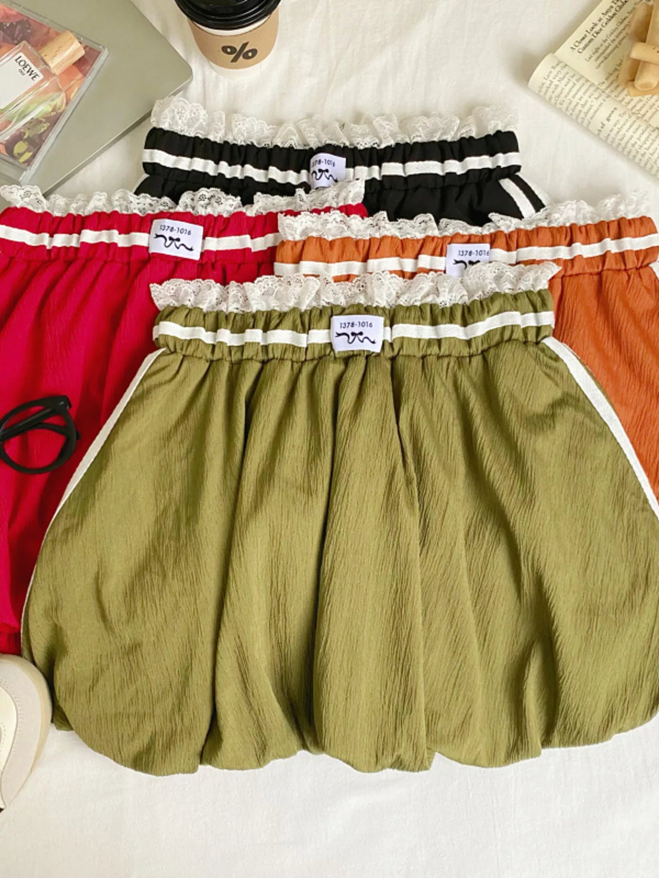 Four pairs of colorful shorts with lace trim on a white surface.