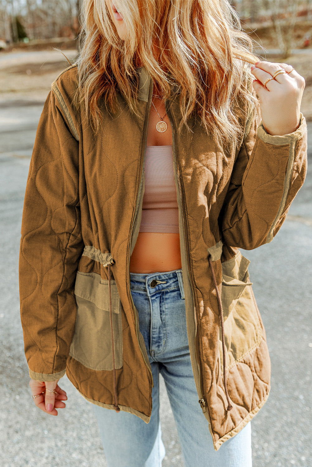 Person wearing a brown jacket, white top, and blue jeans outdoors.