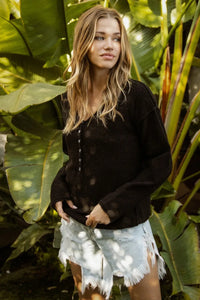 Woman in a black jacket and white shorts standing among large green leaves
