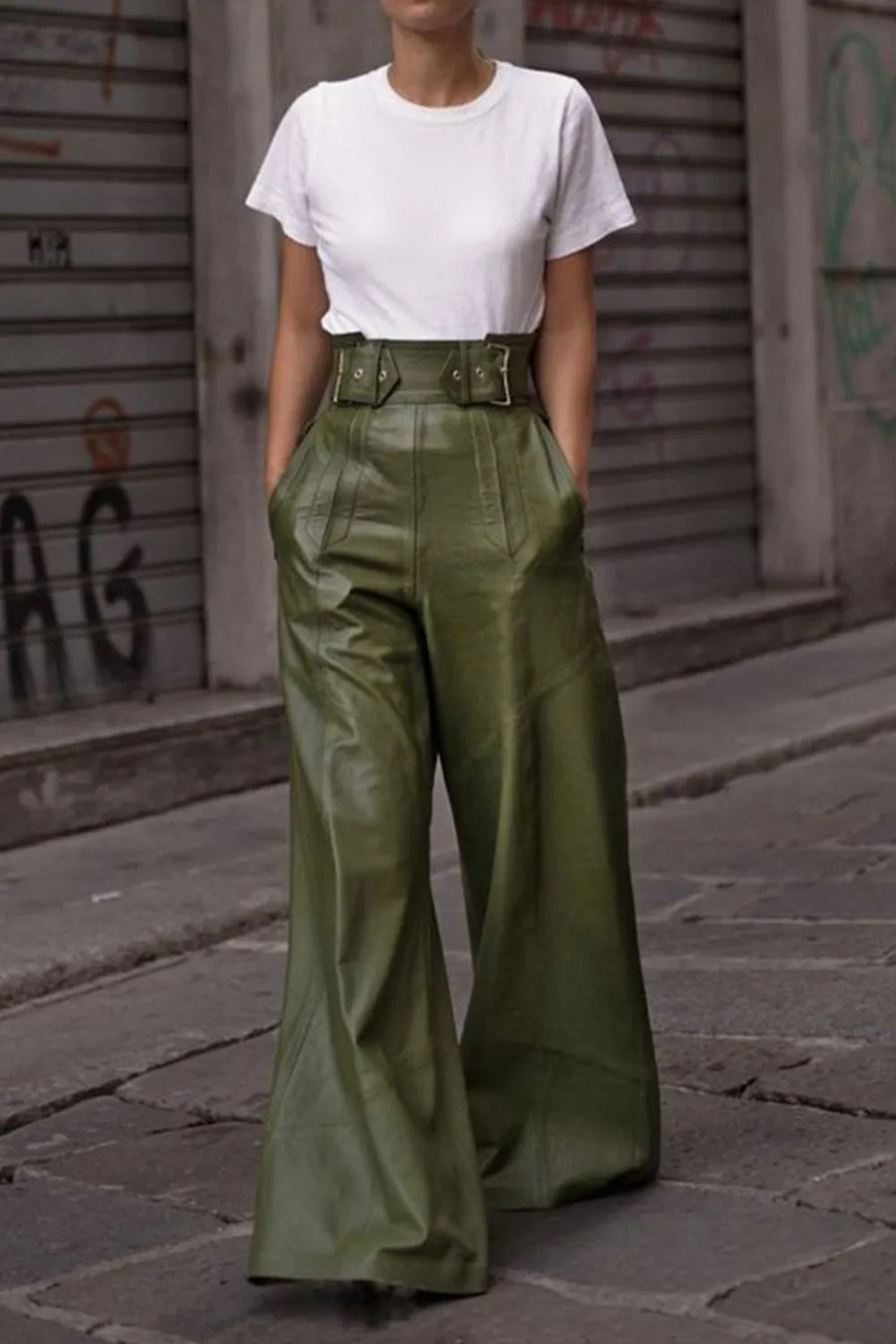 Person wearing a white t-shirt and green leather pants standing on a street with graffiti.